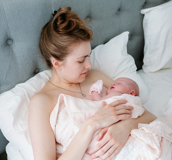 Woman holding newborn baby in bed, reflecting on returning to private office after working from home two years Woman holding newborn baby in bed, reflecting on returning to private office after working from home two years