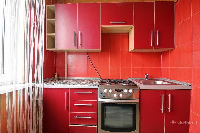 Compact kitchen with red cabinets, red tiled walls, and a stainless steel stove in a wild real estate listing.