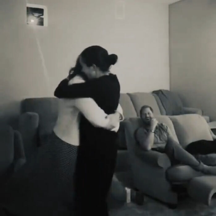 Meghan Markle and Prince Harry sharing a hug during a home celebration, with Prince Harry watching and smiling on the couch. Meghan Markle and Prince Harry sharing a hug during a home celebration, with Prince Harry watching and smiling on the couch.