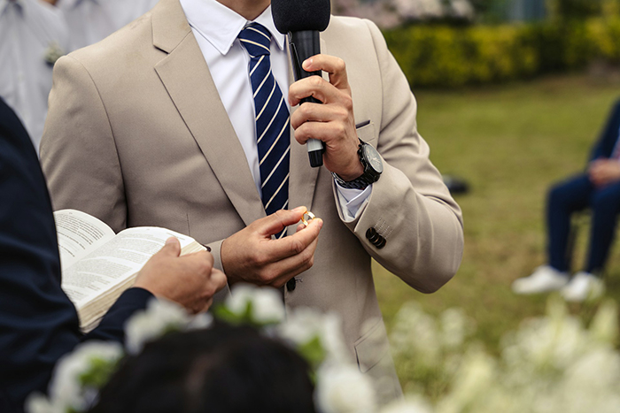 Groom holding wedding ring and microphone during outdoor ceremony, symbolizing vows written with ChatGPT. Groom holding wedding ring and microphone during outdoor ceremony, symbolizing vows written with ChatGPT.