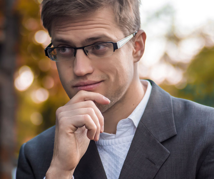 Young man in glasses and suit looking thoughtful outside, symbolizing employee reading handbook to find loophole. Young man in glasses and suit looking thoughtful outside, symbolizing employee reading handbook to find loophole.