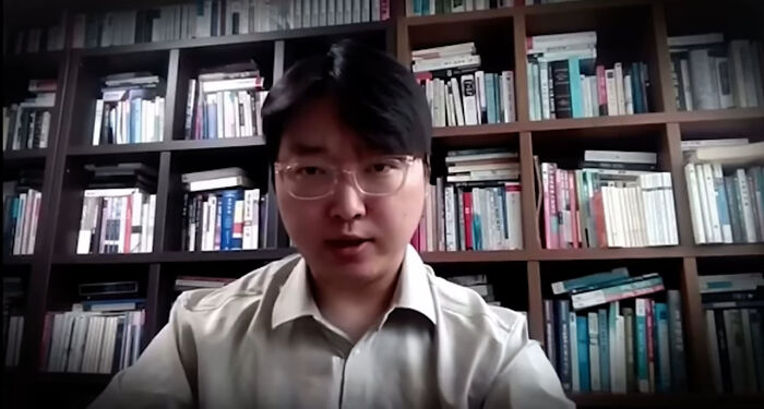 Man wearing glasses and white shirt speaking in front of a bookshelf, related to South Korea asylum and smartest man topic. Man wearing glasses and white shirt speaking in front of a bookshelf, related to South Korea asylum and smartest man topic.