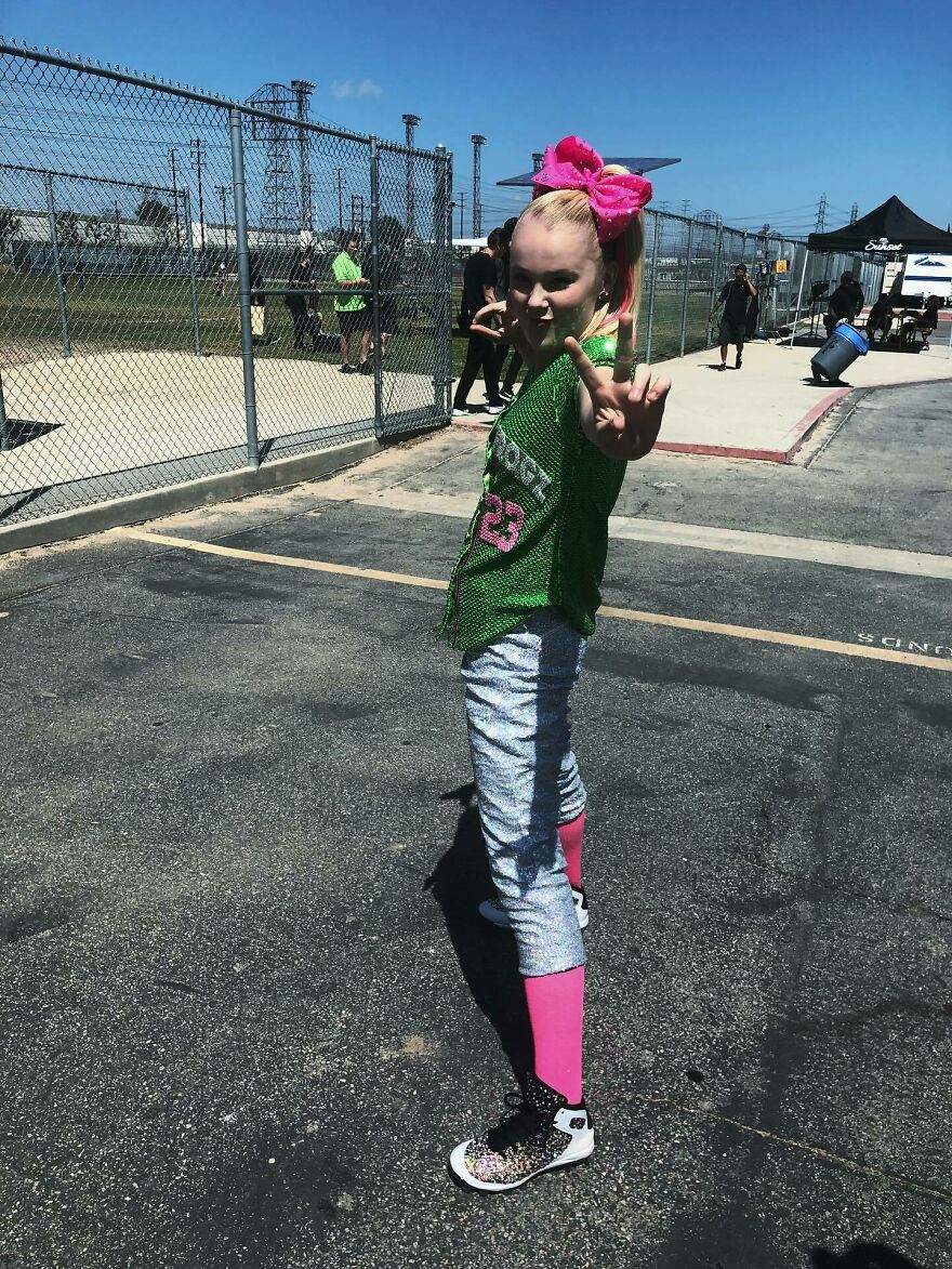 Jojo Siwa posing outdoors wearing a green top and pink accessories highlighting music streams and merch sales success. Jojo Siwa posing outdoors wearing a green top and pink accessories highlighting music streams and merch sales success.