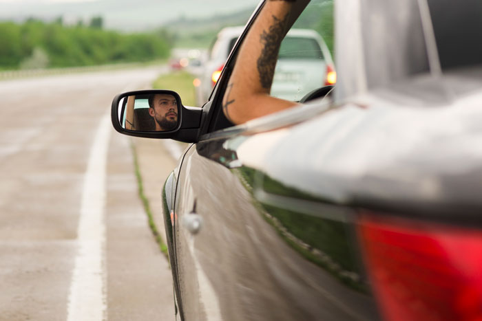 Man looking in car side mirror while driving on highway, capturing a moment of instant karma on the road.