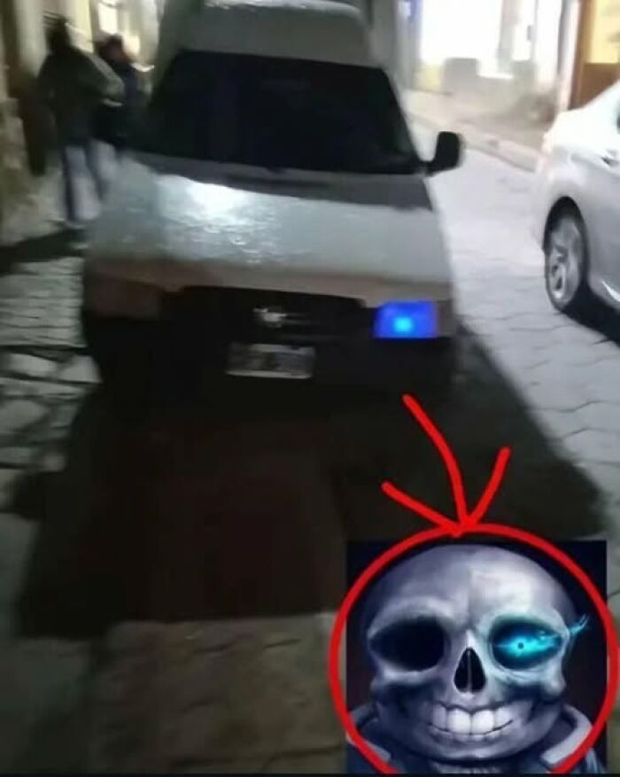 Blurry photo of a car with a blue light on at night and a cartoon skull circled with a red arrow pointing at it.