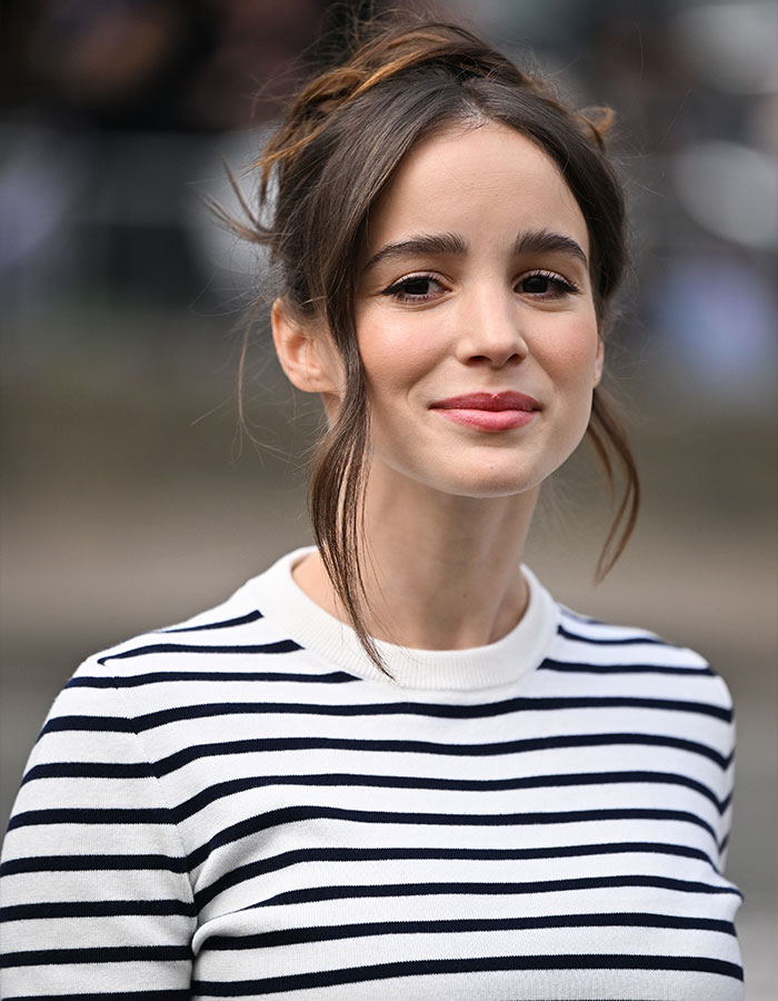 Young woman with hair tied up, wearing a black and white striped shirt, outdoors with a soft smile.