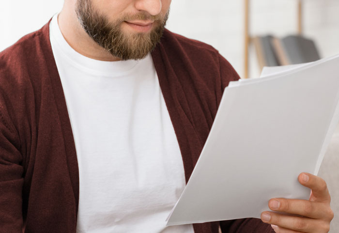 Bearded man in casual clothes reading papers, reflecting on stories about people who don't deserve nice things.