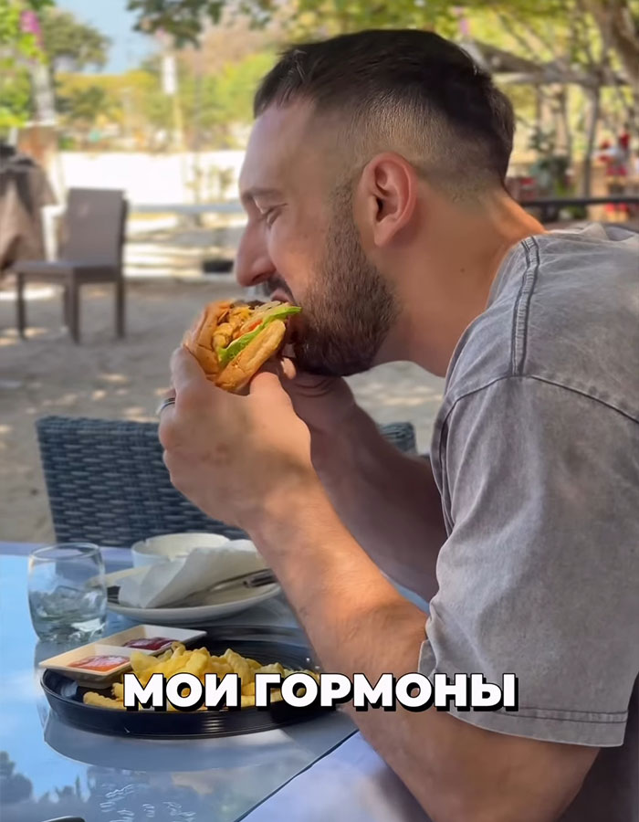 Man biting into a sandwich outdoors, illustrating a binge-eating challenge related to a fitness coach and mayo consumption. Man biting into a sandwich outdoors, illustrating a binge-eating challenge related to a fitness coach and mayo consumption.