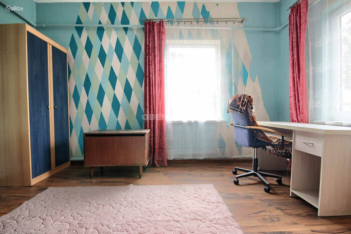 Room with patterned blue walls, mismatched furniture, and pink curtains in a wild real estate listing interior.