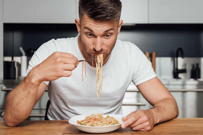 Man eating spaghetti messily in kitchen illustrating lovable things clueless dads did during pregnancy moments