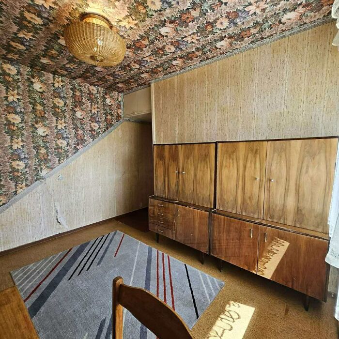 Vintage room with floral wallpaper and wood cabinets in a wild real estate listing with outdated decor and furnishings