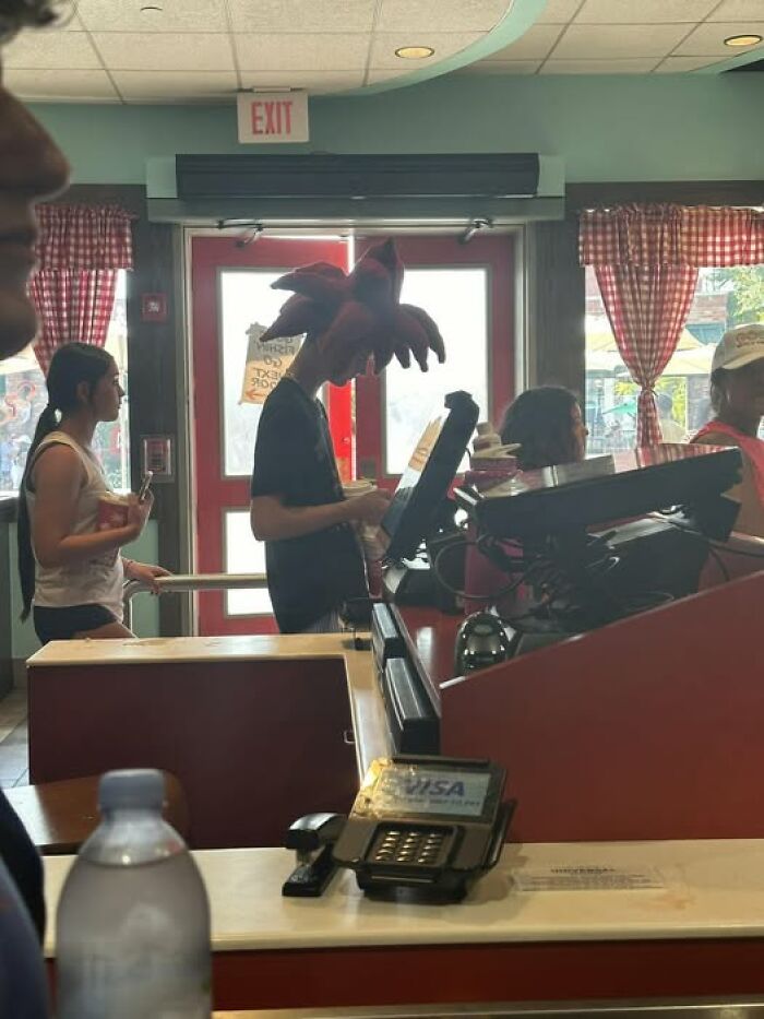 People waiting in line at a counter inside a diner, with one person wearing a striking headpiece in this pics that go hard moment.