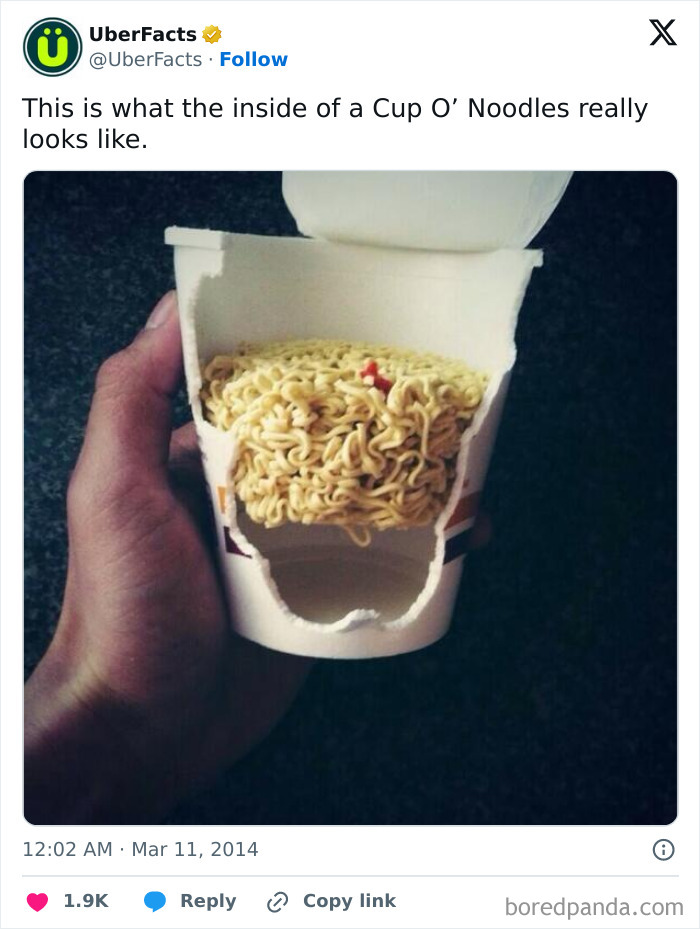 Hand holding a cut-open Cup O’ Noodles showing the inside, revealing the uncooked noodle block inside the container.