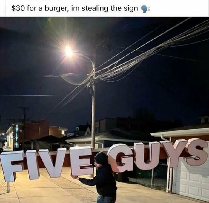 Person stealing a large Five Guys sign at night under a streetlight, fitting the theme of images needing a priest or exorcist.