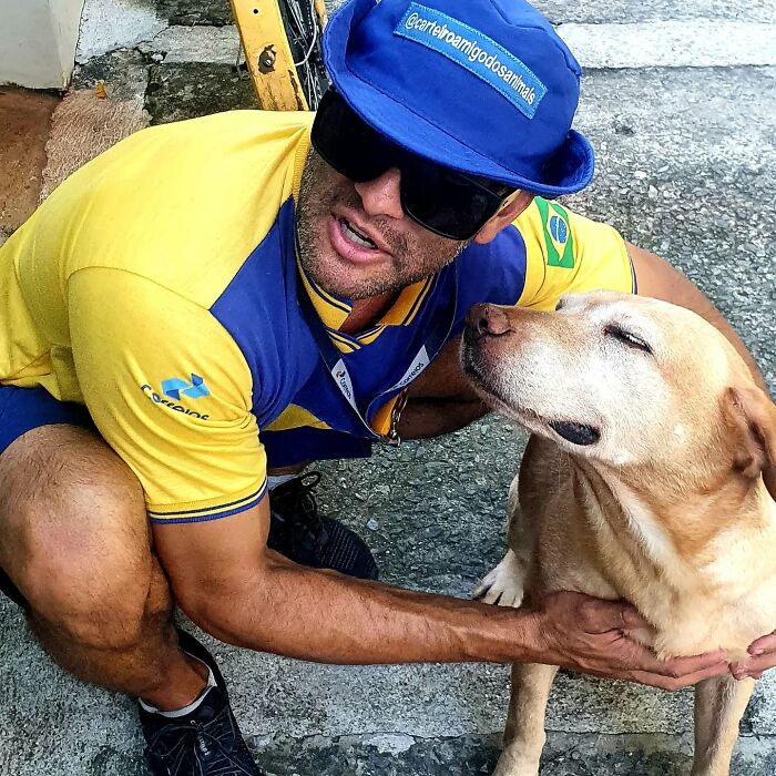 Mailman wearing blue cap and sunglasses smiling while petting a friendly dog on his delivery route outdoors.