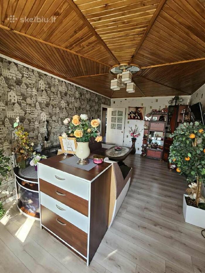 Living room with wooden ceiling, floral wallpaper, and decorative plants in a wild real estate listing interior.