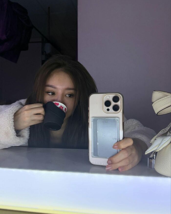 Young woman influencer taking a mirror selfie while drinking from a cup, reflecting provocative influencer lifestyle online. Young woman influencer taking a mirror selfie while drinking from a cup, reflecting provocative influencer lifestyle online.