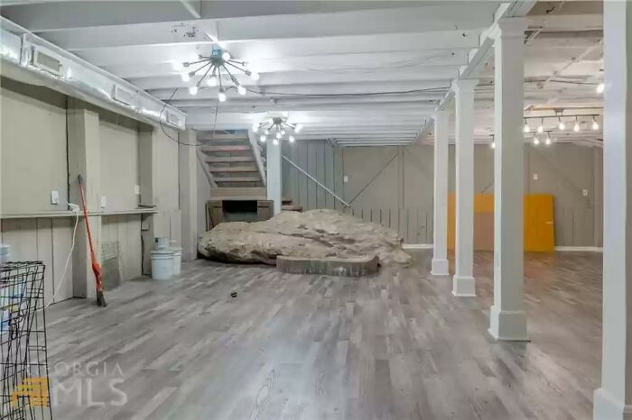 Spacious open basement with exposed beams and a large natural rock feature in a unique Zillow home listing.