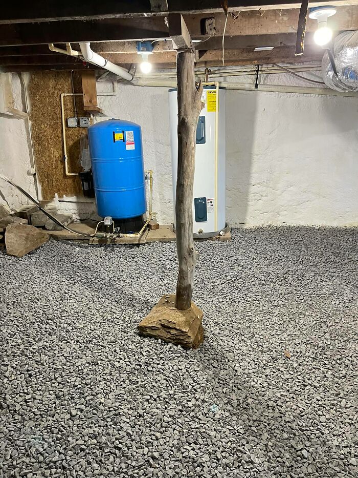 Basement with gravel floor, rustic wooden support beam, water heater and pressure tank in unusual Zillow homes listing.