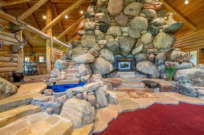 Spacious log cabin interior featuring a large stone fireplace and unique natural rock design in Zillow homes.