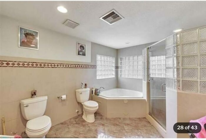 Spacious bathroom in a Zillow home featuring two toilets, a large bathtub, glass block windows, and a glass shower enclosure.