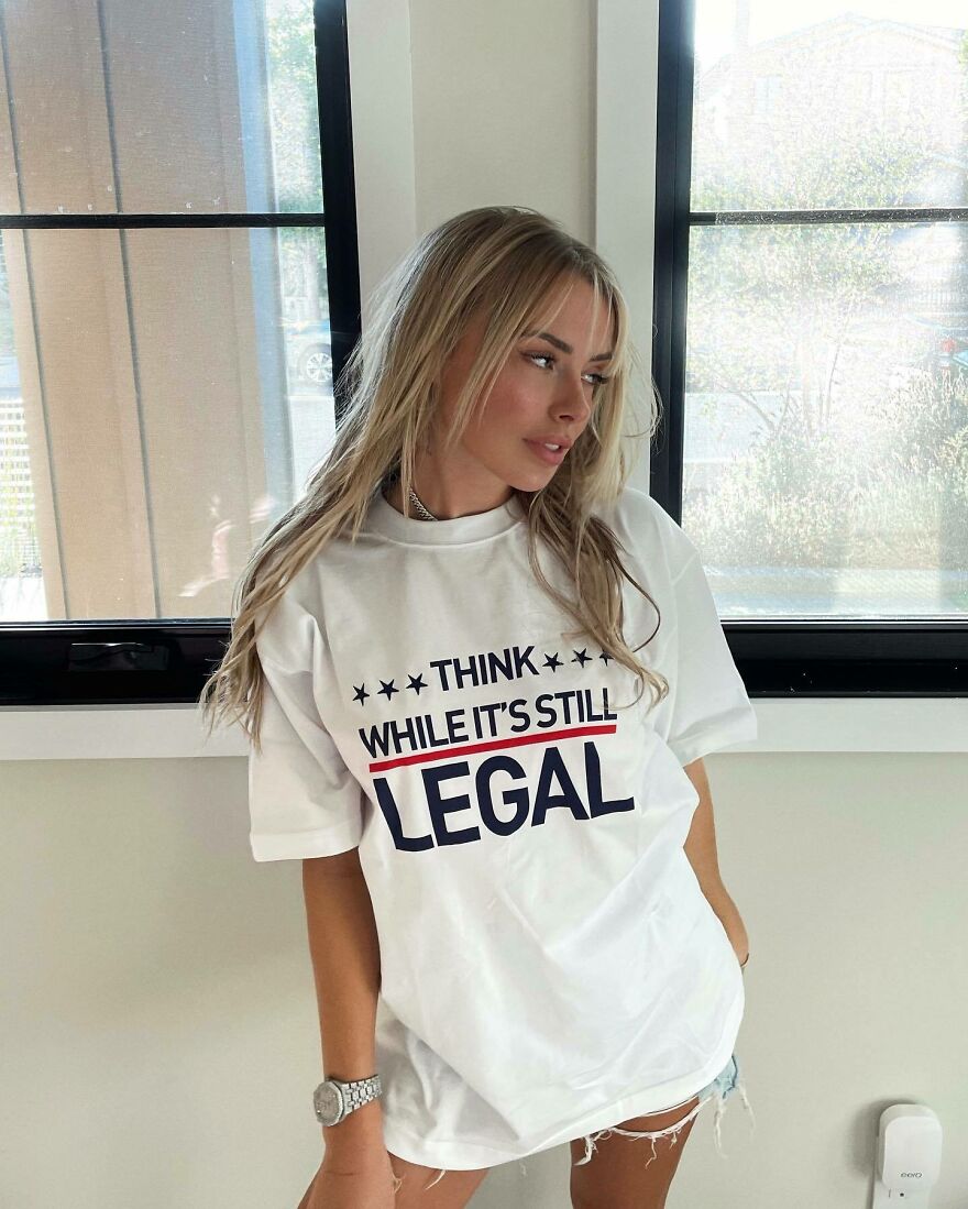 Corinna Kopf wearing a graphic tee indoors next to windows showcasing internet fame and net worth influence.