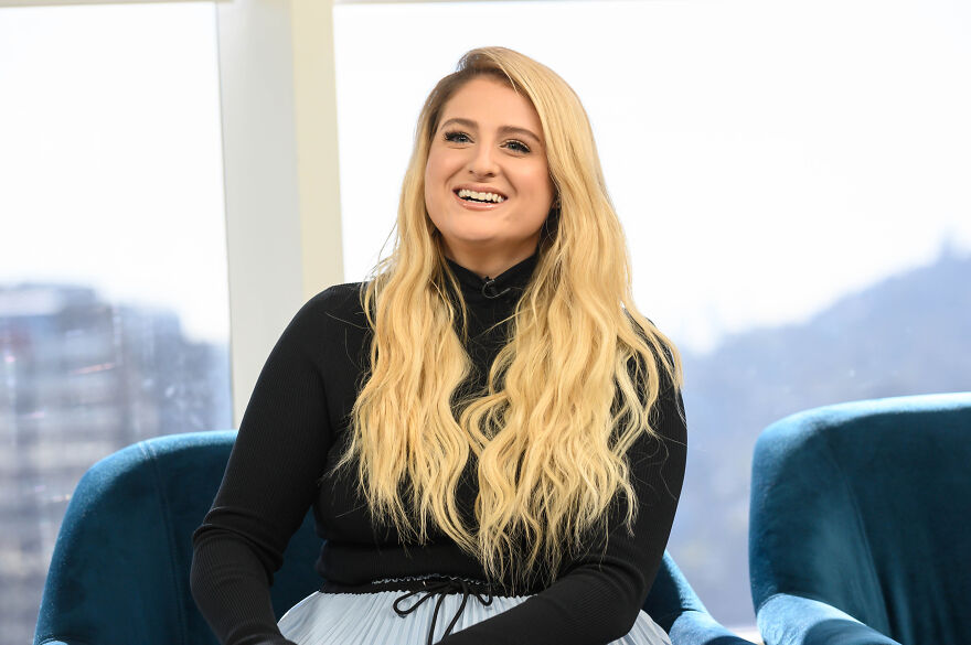 Meghan Trainor smiling during an interview, showcasing her long blonde hair and black top in a modern indoor setting. Meghan Trainor smiling during an interview, showcasing her long blonde hair and black top in a modern indoor setting.