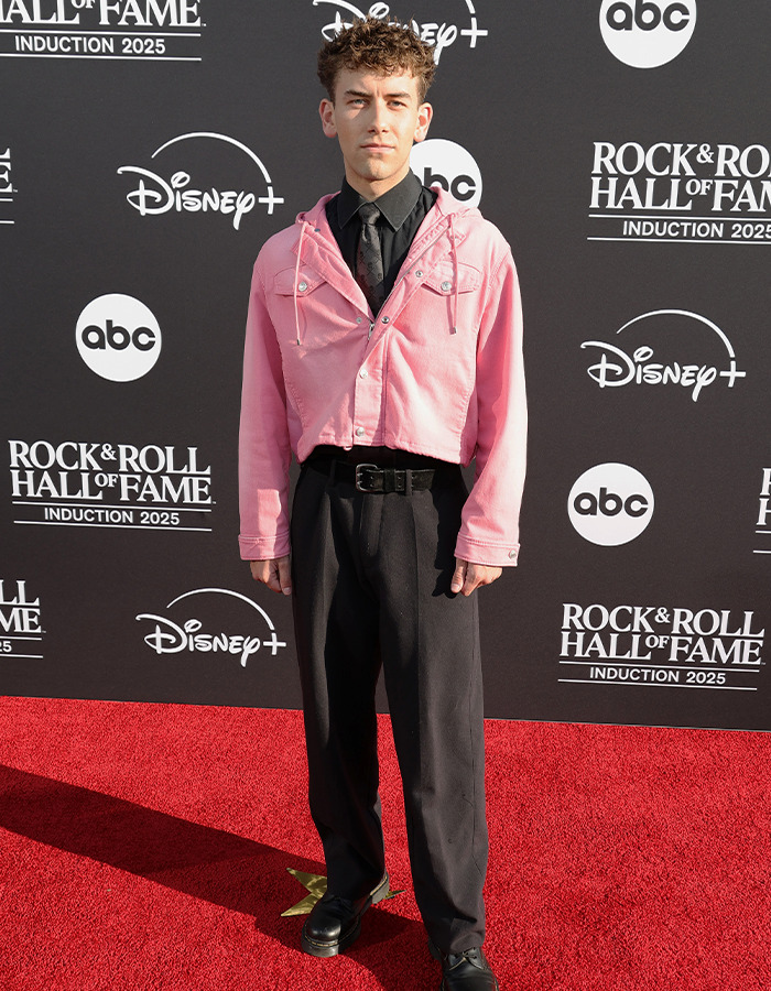 Fashionable attendee in a pink cropped jacket and black pants posing on the red carpet at Rock Hall of Fame 2025 event.