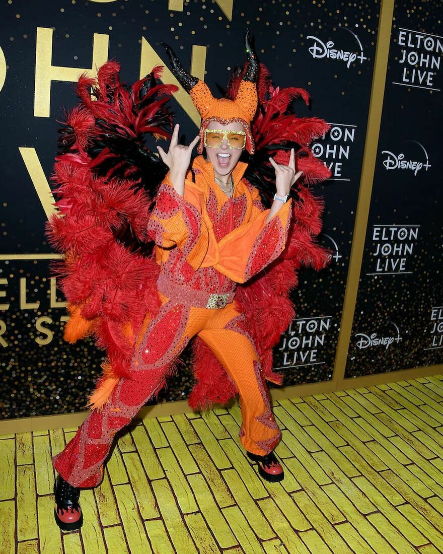 Jojo Siwa in vibrant orange and red feathered costume posing energetically, representing music streams and merch sales impact. Jojo Siwa in vibrant orange and red feathered costume posing energetically, representing music streams and merch sales impact.