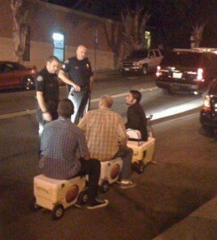 Three men sitting on coolers in the street talking to two police officers in a night scene, funny pics that go hard.