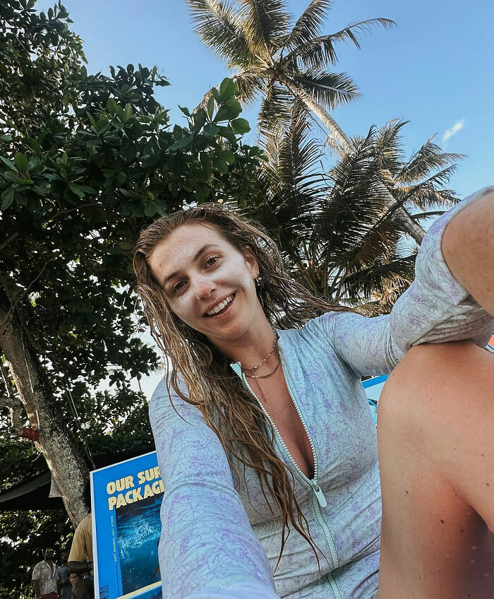 Woman solo traveling outdoors with palm trees in background, smiling and taking a selfie in casual beachwear. Woman solo traveling outdoors with palm trees in background, smiling and taking a selfie in casual beachwear.