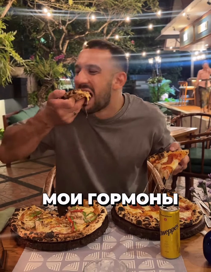 Man eating multiple large pizzas at outdoor restaurant, related to fitness coach binge-eating challenge involving mayo. Man eating multiple large pizzas at outdoor restaurant, related to fitness coach binge-eating challenge involving mayo.