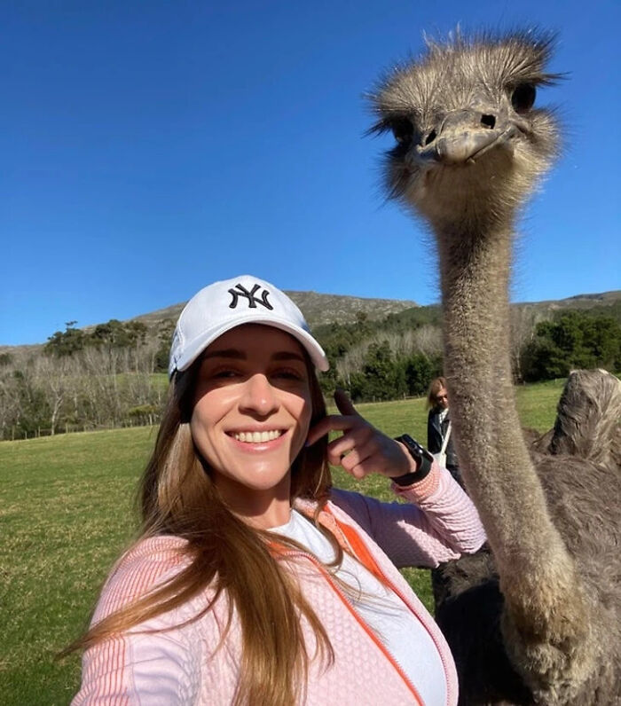 Woman smiling outdoors next to an ostrich posing for a selfie with animals capturing better selfies.