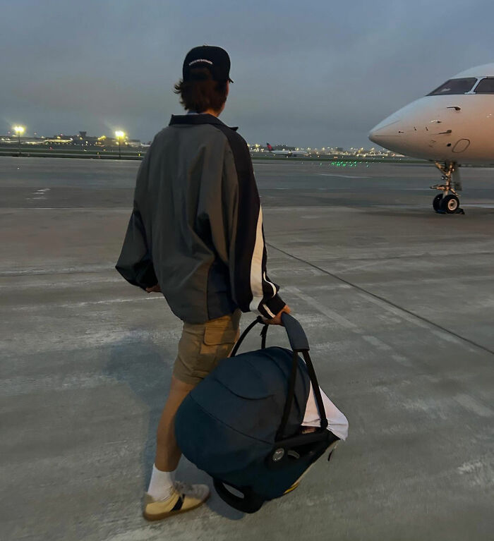 Person walking on airport tarmac at dusk holding a baby car seat near a parked private jet, raising eyebrows online. Person walking on airport tarmac at dusk holding a baby car seat near a parked private jet, raising eyebrows online.