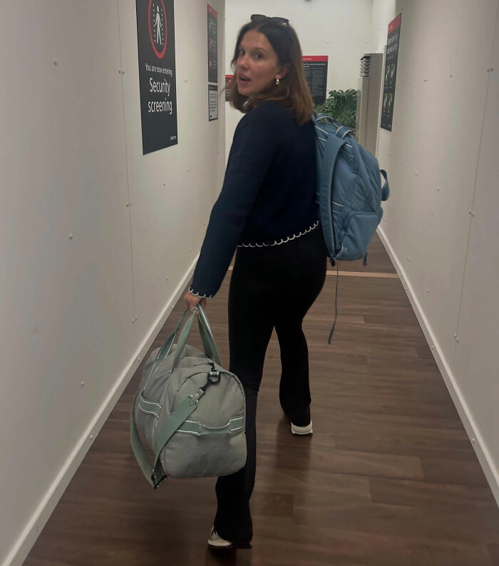 Woman walking down hallway carrying bag and backpack, raising eyebrows linked to Millie Bobby Brown and Jake Bongiovi news. Woman walking down hallway carrying bag and backpack, raising eyebrows linked to Millie Bobby Brown and Jake Bongiovi news.
