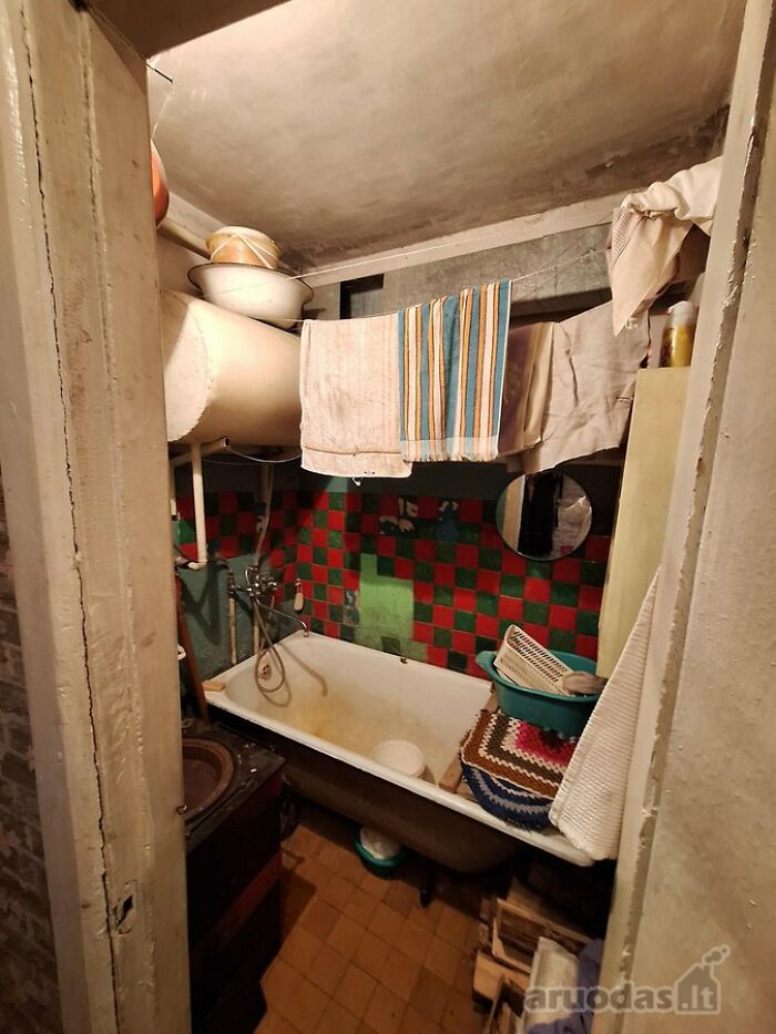 Small cluttered bathroom in real estate listing with old bathtub, colorful tiles, towels hanging, and various household items.