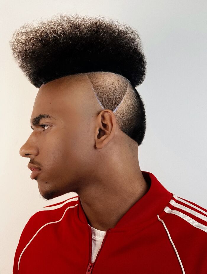 Young man with a bold barber haircut styled into a star shape, wearing a red Adidas jacket and smiling with eyes closed