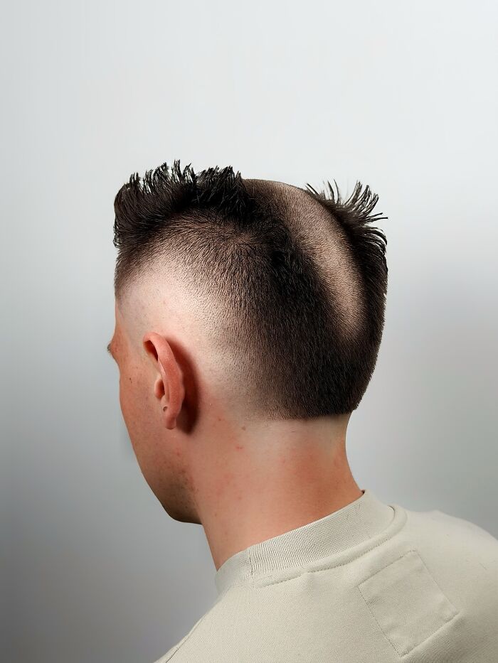 Man with a bold barber haircut featuring a unique styled top and shaved sides against a plain background