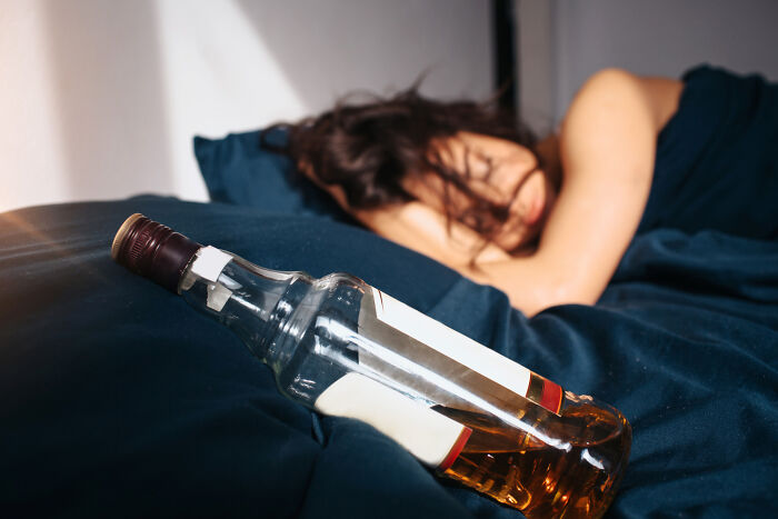 Empty whiskey bottle on a bed near a person lying down, illustrating stories of people who messed up and learned their lesson.