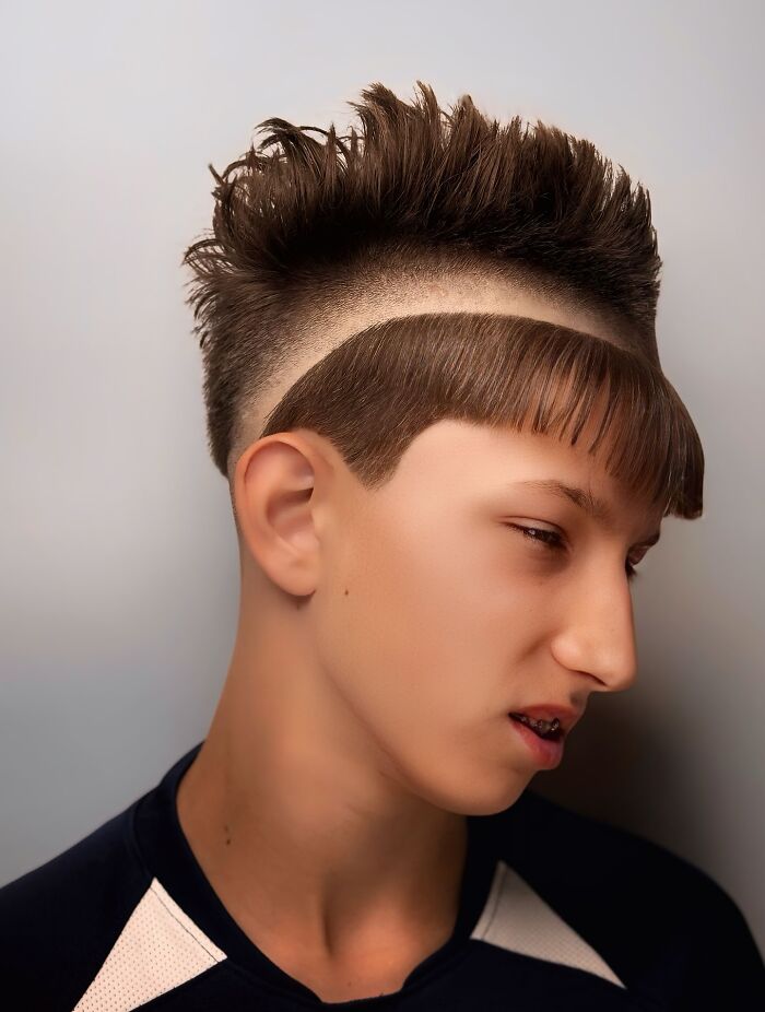 Teen boy with bold barber haircut featuring spiked top and distinct curved fringe line design on sides