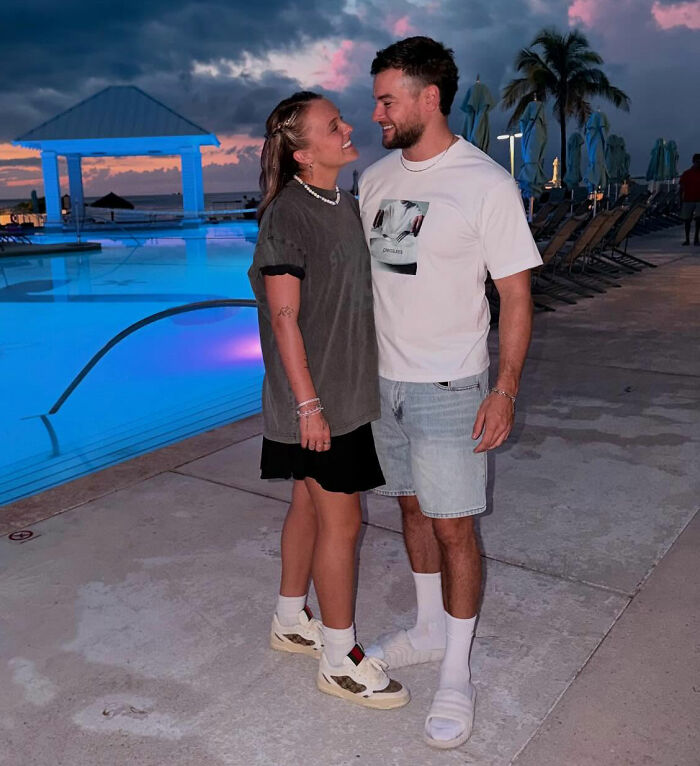 Chris Hughes and a woman smiling and standing near a pool at sunset, JoJo Siwa's fans stunned by reality TV confession. Chris Hughes and a woman smiling and standing near a pool at sunset, JoJo Siwa's fans stunned by reality TV confession.
