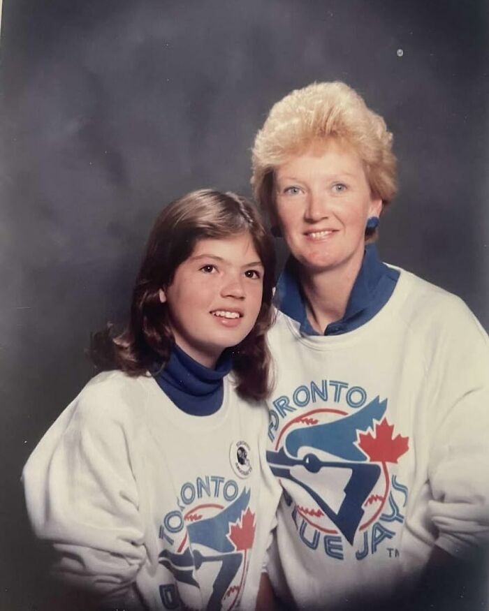 Mother and daughter wearing matching Toronto Blue Jays sweatshirts in an awkward studio picture.
