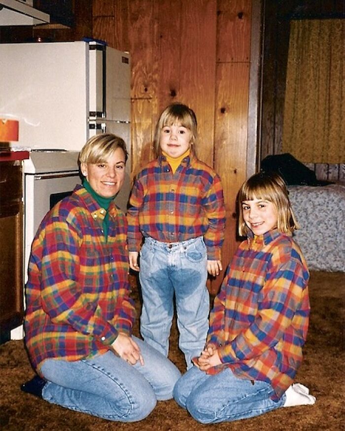 Three people in matching plaid shirts and jeans posing awkwardly in a home studio setting with wood paneling.