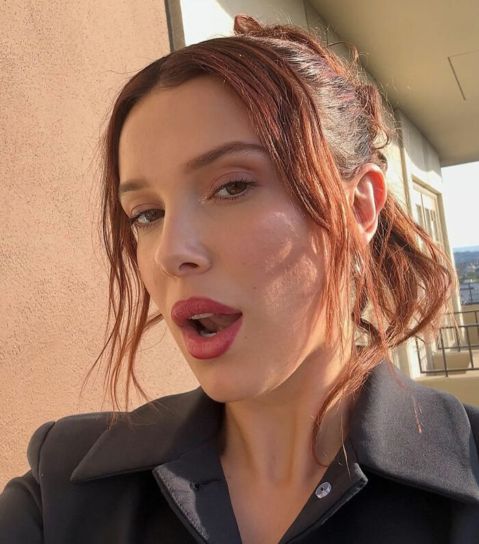 Young woman with red hair styled up, wearing dark clothing, posing outdoors in natural light highlighting lingerie with a train concept.