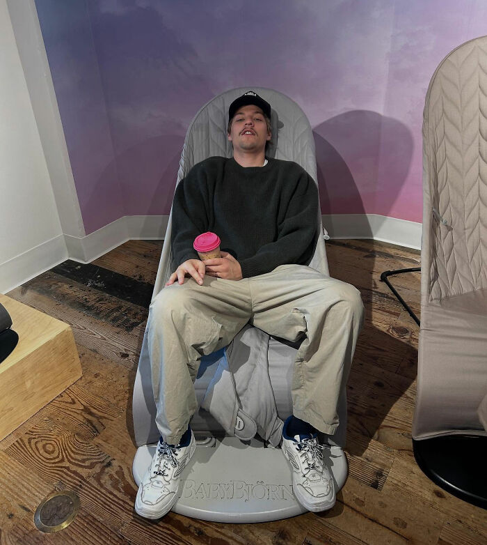 Young man in casual clothes sitting relaxed in a BabyBjorn chair, holding a coffee cup indoors. Young man in casual clothes sitting relaxed in a BabyBjorn chair, holding a coffee cup indoors.