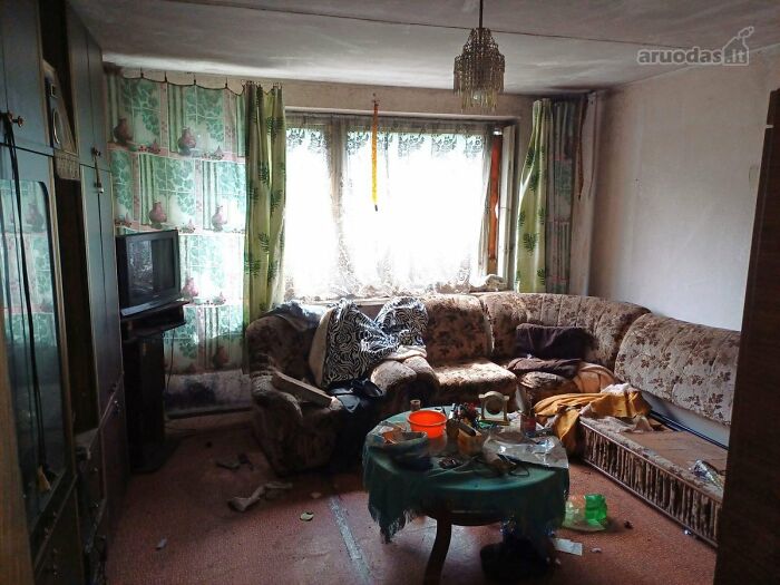 Cluttered and outdated living room in wild real estate listing with worn furniture and dim lighting.