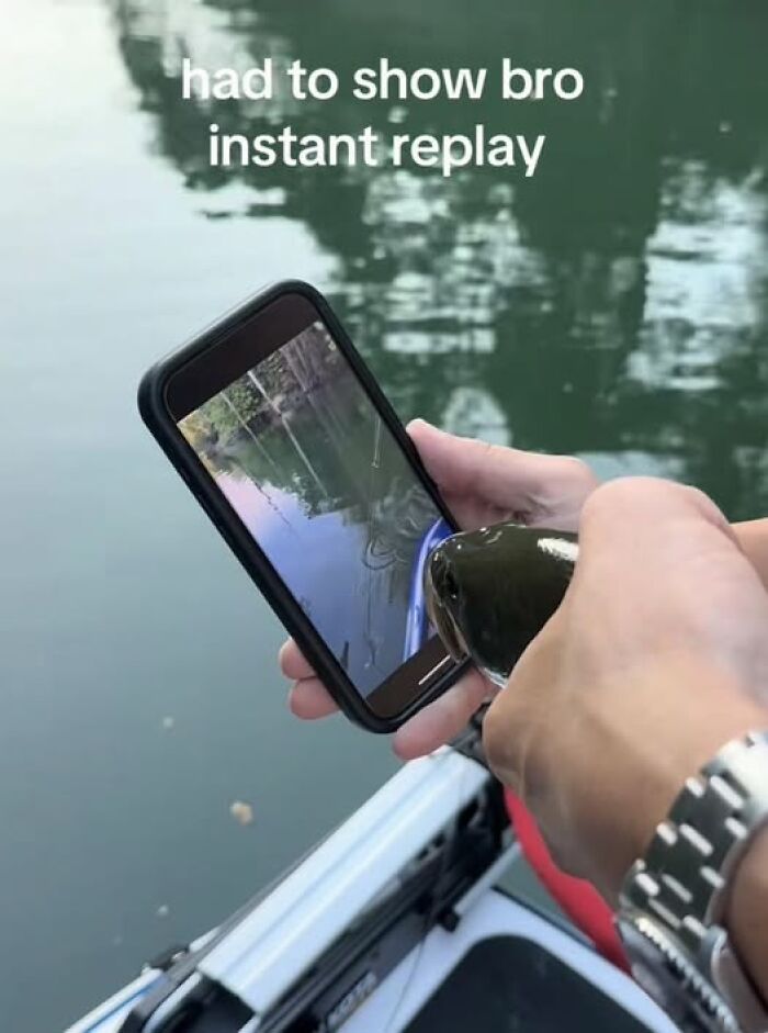 Person holding a fish and phone showing an instant replay while fishing, a popular pic that goes hard.