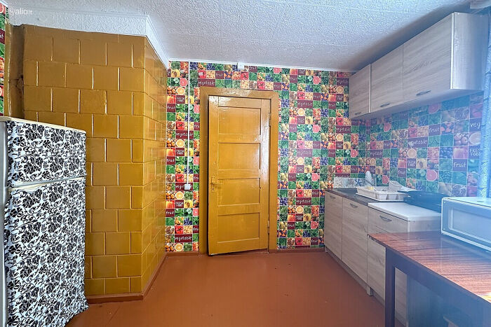 Kitchen with wild real estate listing featuring colorful fruit and vegetable wallpaper and a mustard yellow door and tiles.