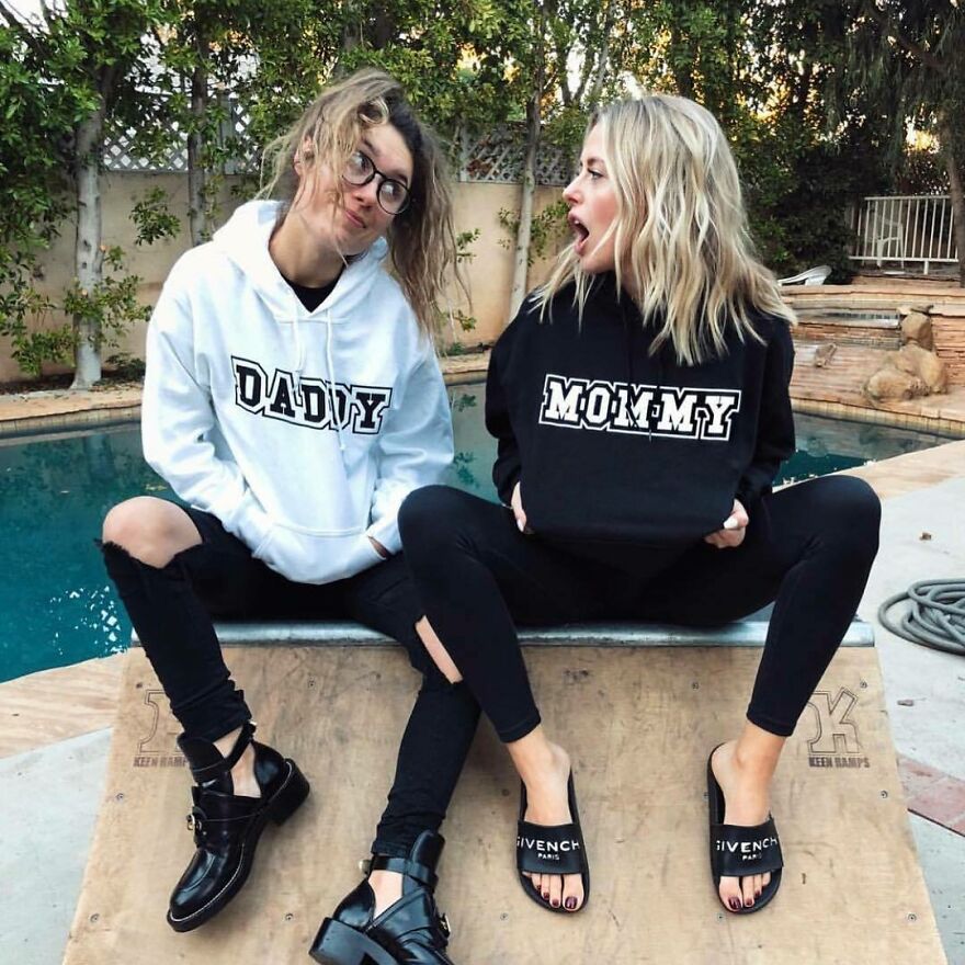 Two women wearing hoodies with daddy and mommy text, sitting by a pool, representing internet fame and Corinna Kopf net worth.