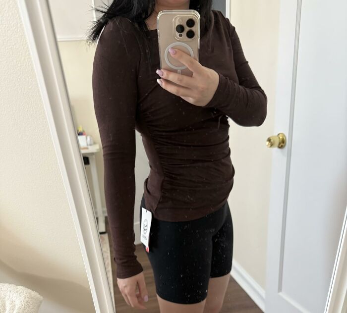Woman wearing a brown long-sleeve top and black shorts from Alix Earle’s Amazon store showing a tagged outfit in a mirror selfie